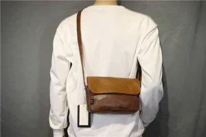 Detail view of a retro Japanese minimalist flap messenger bag worn crossbody, brown leather.