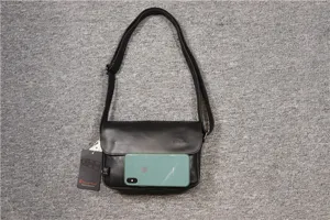 Detail shot of black leather messenger bag with flap, adjustable strap and metal hardware details.