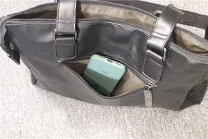 Detailed view of black leather business briefcase with front zip pocket and phone display.