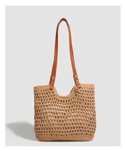 Detailed view of the woven straw tote bag featuring brown leather shoulder straps and open top.