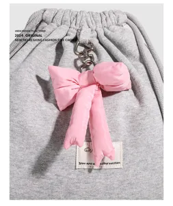 Gros-plan du pendentif nœud rose et du fermoir cœur sur le sac à dos gris détail.