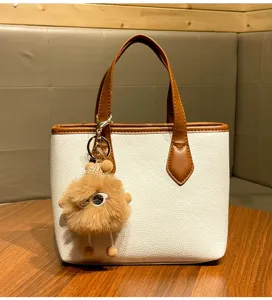 Detailed view of the white and brown litchi grain tote bag with cute fluffy plush keychain.