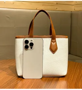 Detail view of a stylish white litchi pattern bucket bag with brown handles for daily commute.
