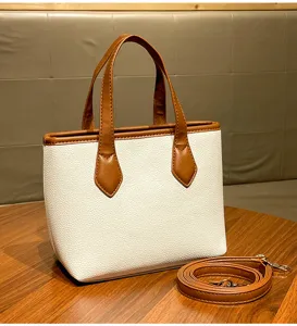 Detail view of white pebbled bucket bag with brown handles and strap on wooden table scene.