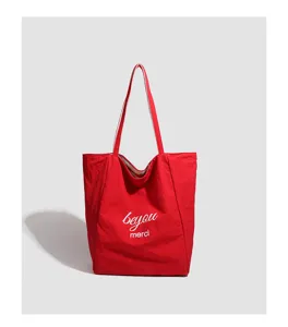 Red canvas tote bag detail, featuring white printed lettering and comfortable shoulder strap.