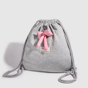 Sac a dos coulissant gris minimaliste pour femme avec pendentif noeud rose pour usage quotidien.