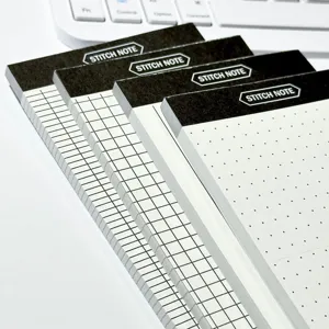Detail shot of four sticky note pads with grid dot and line pages on white desk.