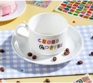 Ceramic coffee cup and saucer set with colorful letters detail view in a bright lifestyle scene.