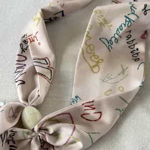 Closeup view of pink silk twilly scarf with colorful handwriting print and magnetic clasp.