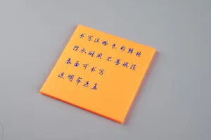 Détail de note adhésive transparente orange montrant une surface étanche et inscriptible.