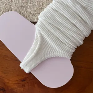 Close-up of white knitted stirrup leg warmers showcasing fine ribbed texture and fabric detail.