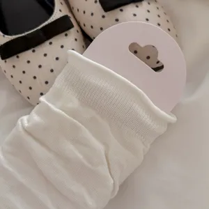 Detailed view of white knitted leg warmers with folded cuffs, soft slouchy fabric texture.