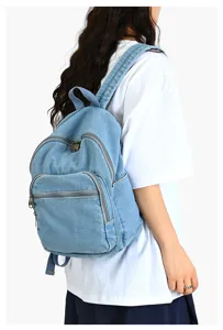 Vue détaillée latérale d'un sac à dos en jean bleu clair porté par un mannequin.