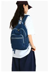 Gros plan sur le sac a dos en denim bleu montrant sa texture en toile et ses fermetures eclair.