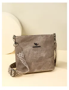 Detail shot of the brown canvas crossbody bag featuring a wide patterned strap and metal logo.