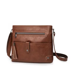 Detail view of brown PU leather crossbody bag featuring metal zipper, tassel and front pocket.