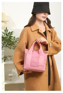 Close-up view of a cute pink canvas tote bag held by a model, showing sturdy handles and pocket.