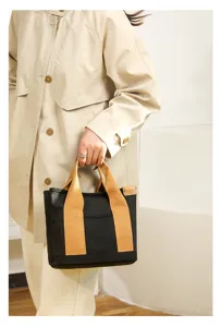Black canvas tote bag with tan handles, casual minimalist style handbag for daily commute use.