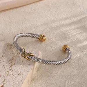 Detailaufnahme eines silbernen Kabelarmreifs mit goldenen Enden und funkelnder Strass X-Form.