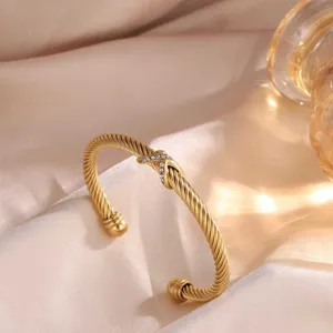 Detailaufnahme des luxuriösen verdrehten Stahlarmbands mit glänzendem Kristall X Motiv.