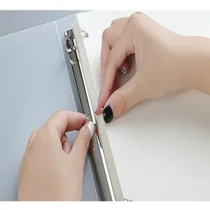Close-up detail shot of hands opening the metal loose-leaf binder rings on a grid notebook.