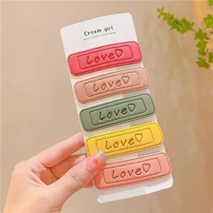 Close-up view of colorful leather hair clips showing love embroidery and backing card details.