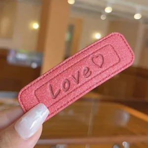 Close-up detail of pink leather hair clip with embossed love text and stitching accent.