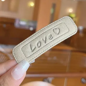 Close-up detail of chic leather hair clip featuring embossed love text and a sweet heart pattern.