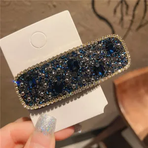 Close-up detail of a sparkly rhinestone hair clip with dark blue crystals and silver base.