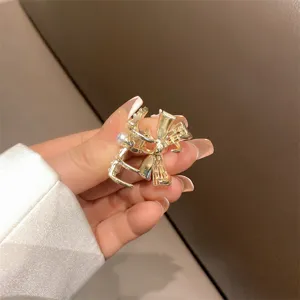 Dettaglio molletta per capelli a fiocco dorato, piccola clip metallica con perla.