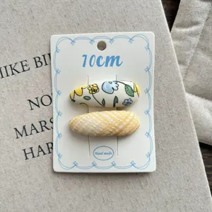 Detailed shot of yellow fabric hair clips with floral and plaid patterns, 10cm size.