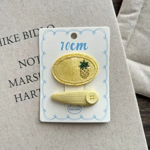 Cream yellow fabric hair clips detail showing pineapple embroidery and cute button decoration.
