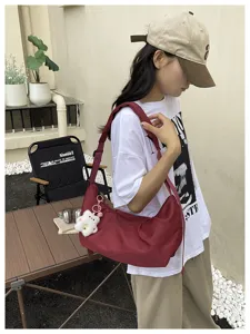 Detailed shot of a stylish burgundy nylon hobo bag worn outdoors with cute bear pendant.