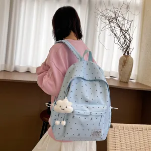 Détail de sac à dos bleu clair avec motif nœud, poche avant et pendentif peluche nuage.