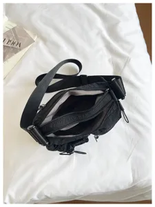 Black nylon crossbody bag detail showing multiple zip compartments and adjustable strap.