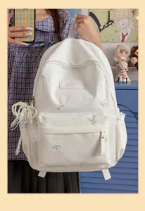 Detail view of the white backpack featuring colorful bow embroidery and pearl lace pendant accessory.