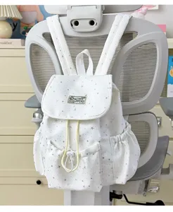 Close-up of a white star-printed backpack hanging on a grey chair, showing front pockets.