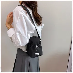 Detail shot of stylish black mini shoulder bag worn by model, featuring handy drawstring design.