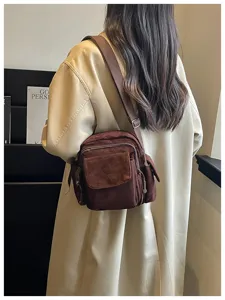 Vue détaillée du sac bandoulière marron en suédine porté avec un manteau trench élégant.