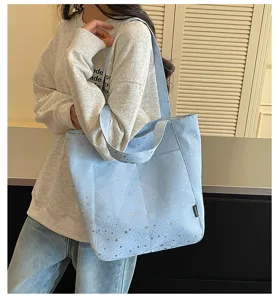 Detail shot of a minimalist light blue tote bag with silver star prints and dual handles.