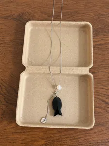 Detailed shot of the black fish pendant necklace with white bead and delicate heart charm.