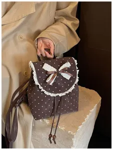 Detail shot of brown polka dot mini backpack with cute white lace ruffle and bow decoration.