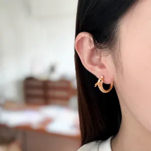 Vue détaillée d'une délicate boucle d'oreille créole serpent plaquée or avec zirconiums brillants.
