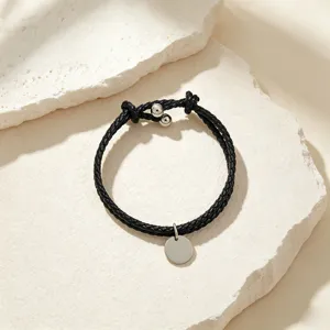 Detailed close-up of a stylish black braided leather bracelet featuring a sleek metal round pendant.