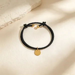 Elegant black braided leather bracelet with a minimalist gold round pendant and chic ball ends.
