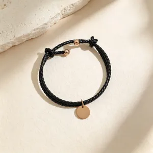 Black braided leather bracelet with a rose gold round pendant, delicate and stylish jewelry detail.