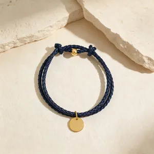 Close-up detail shot of dark blue braided leather cord bracelet with gold-tone round pendant.