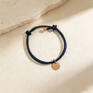 Close-up detail of a navy blue braided leather bracelet with gold-tone round tag and beads.