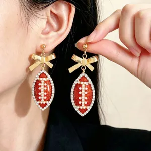 Close-up detail of football dangle earrings with rhinestones, pearls, and gold bow design.