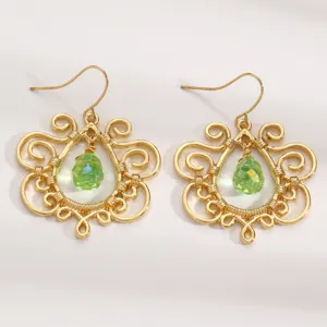Detailed close-up of retro gold-toned filigree hollow earrings with green teardrop crystal drop.